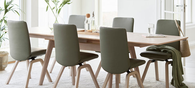 Stressless eetkamerstoelen in grijsgroene stof rond een lange eiken Stressless-eettafel in een lichte eetkamer