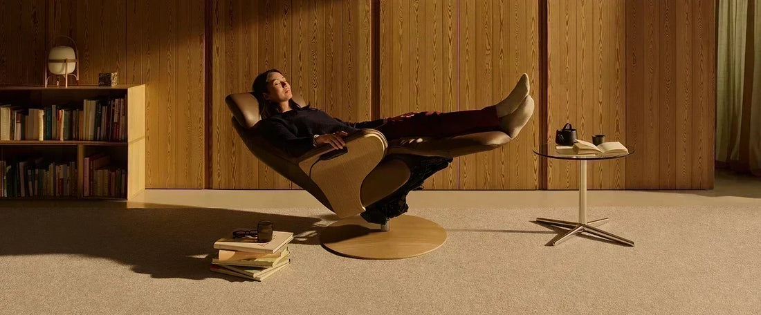Vrouw ontspant achterover in een lederen Stressless relaxfauteuil met uitgeklapte voetensteun, in een sfeervolle leeshoek met houten wandpanelen en boekenkast.