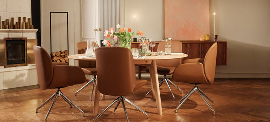 Stressless Bay eetkamerstoelen in cognacbruin leder op draaibare stervoeten rond een gedekte ronde tafel bij de open haard