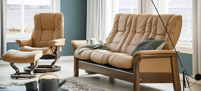 Stressless relaxzetel met voetenbank in beige leder naast een bijpassende Stressless Windsor-zitbank in een lichte woonkamer