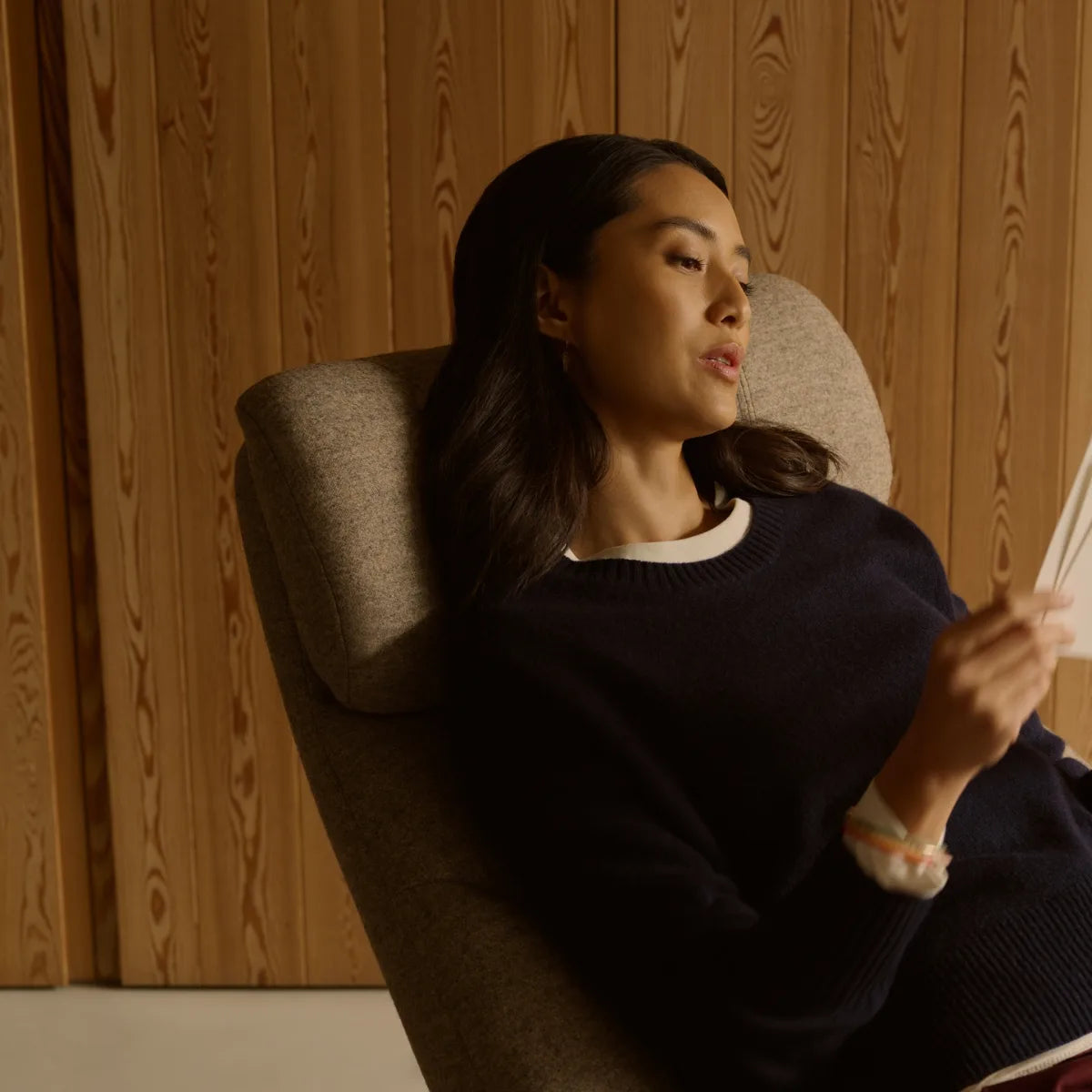 A woman is reading a book in a Stressless Adam, her head resting against the headrest, which tilts forward with her