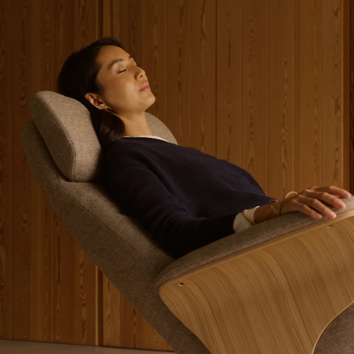 A woman rests with her eyes closed in a Stressless Adam with wooden side panels, winner of the 2025 Red Dot Award