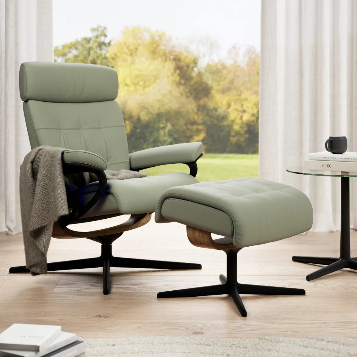 Fauteuil relax Stressless Erik avec repose-pieds, en cuir Paloma Shadow Green sur un piètement Cross, dans un salon lumineux doté d'une grande fenêtre
