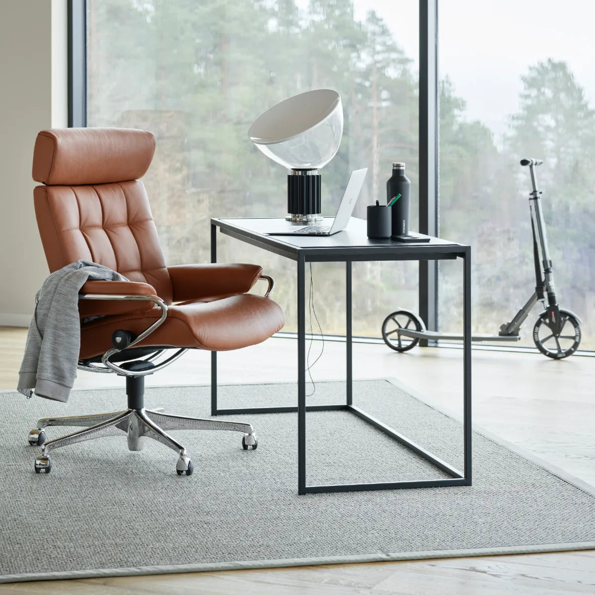 Stressless London Home Office met hoge rug in roodbruin leder op een verchroomd onderstel met wieltjes, aan een bureau