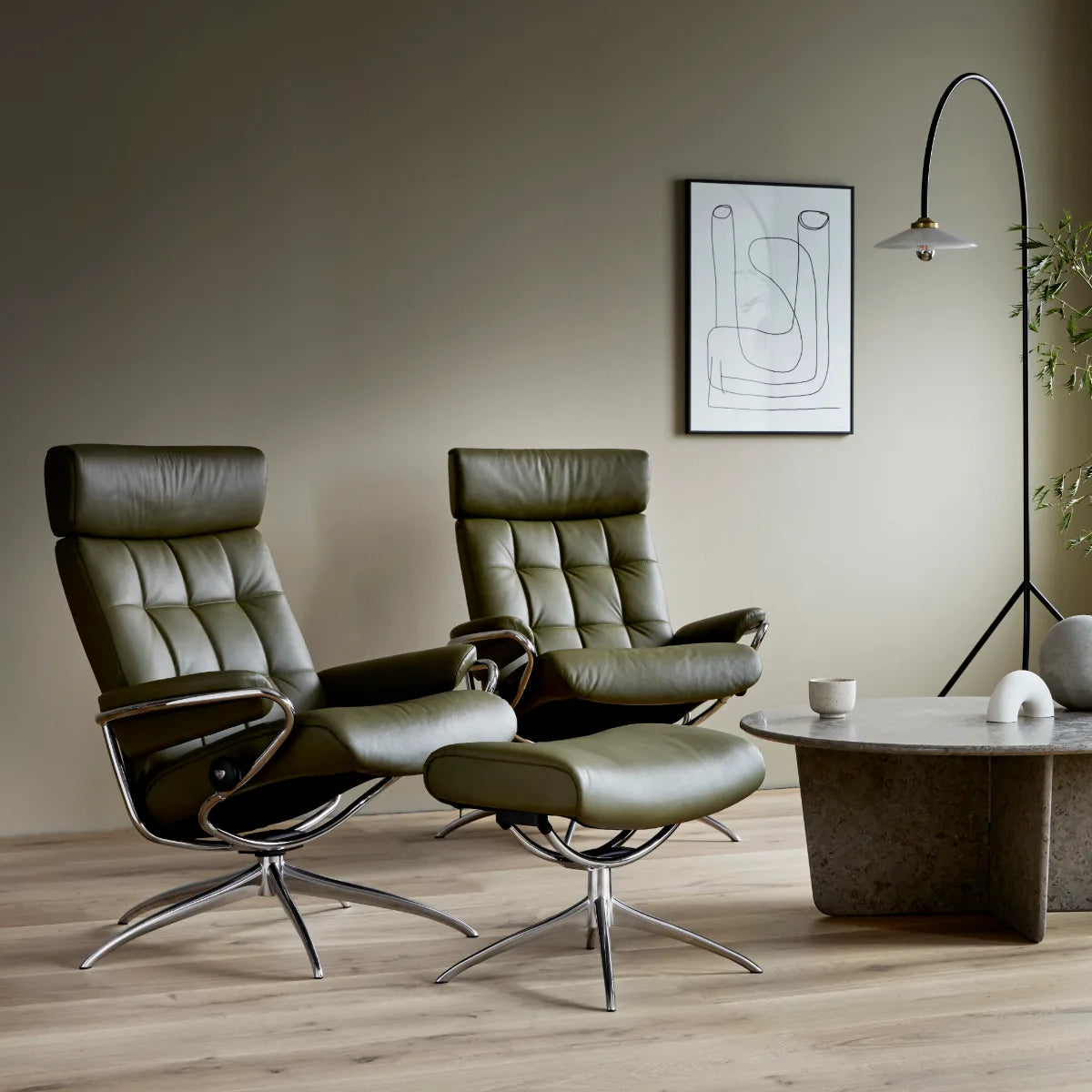 Twee Stressless London relaxfauteuils met verstelbare hoofdsteun in donker leder met voetenbank, naast een salontafel