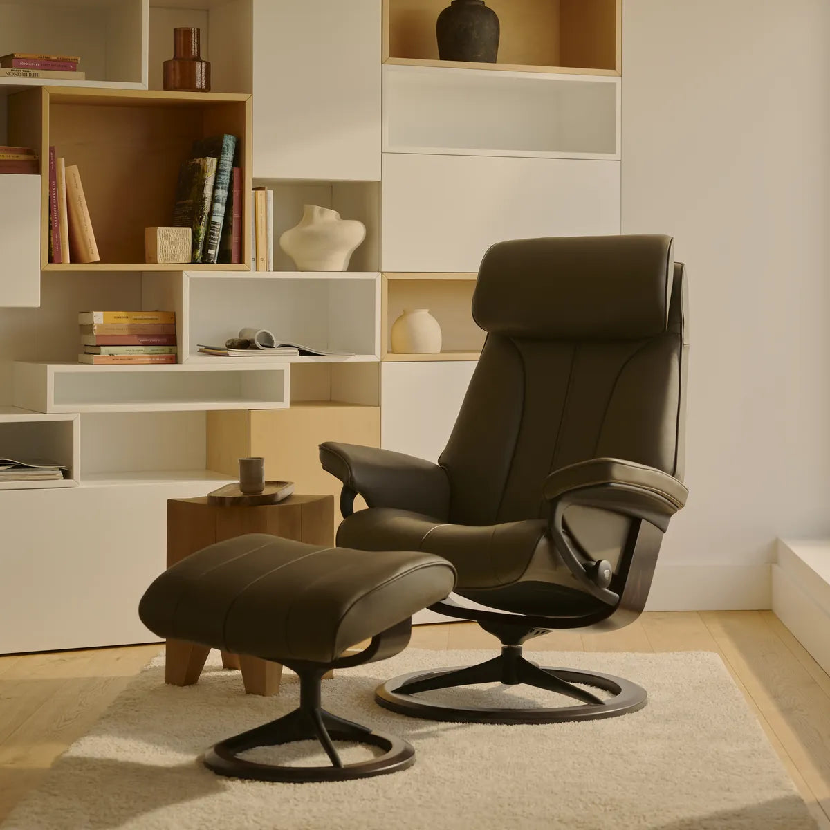 Stressless Paul recliner with footstool in Velaro Forest Green leather on a Signature base with walnut, in a living room with a bookcase