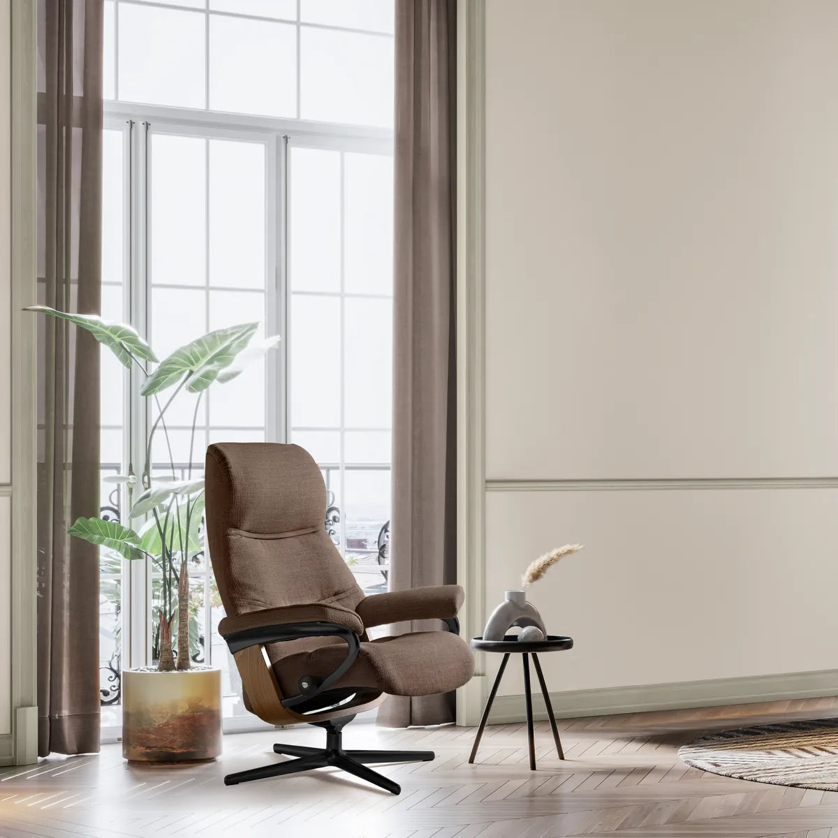 Stressless Philip in caramel-colored fabric on a Cross base, in a high-ceilinged room with a large window and a plant