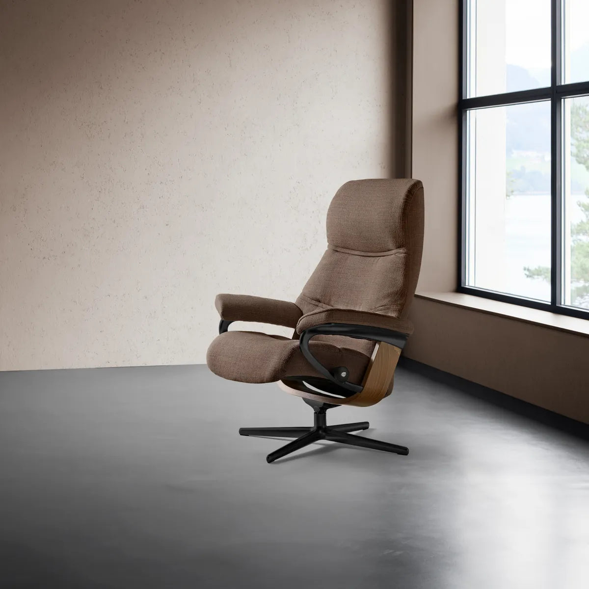 Stressless Philip in caramel-colored fabric on a matte black Cross base, next to a large window in a minimalist space