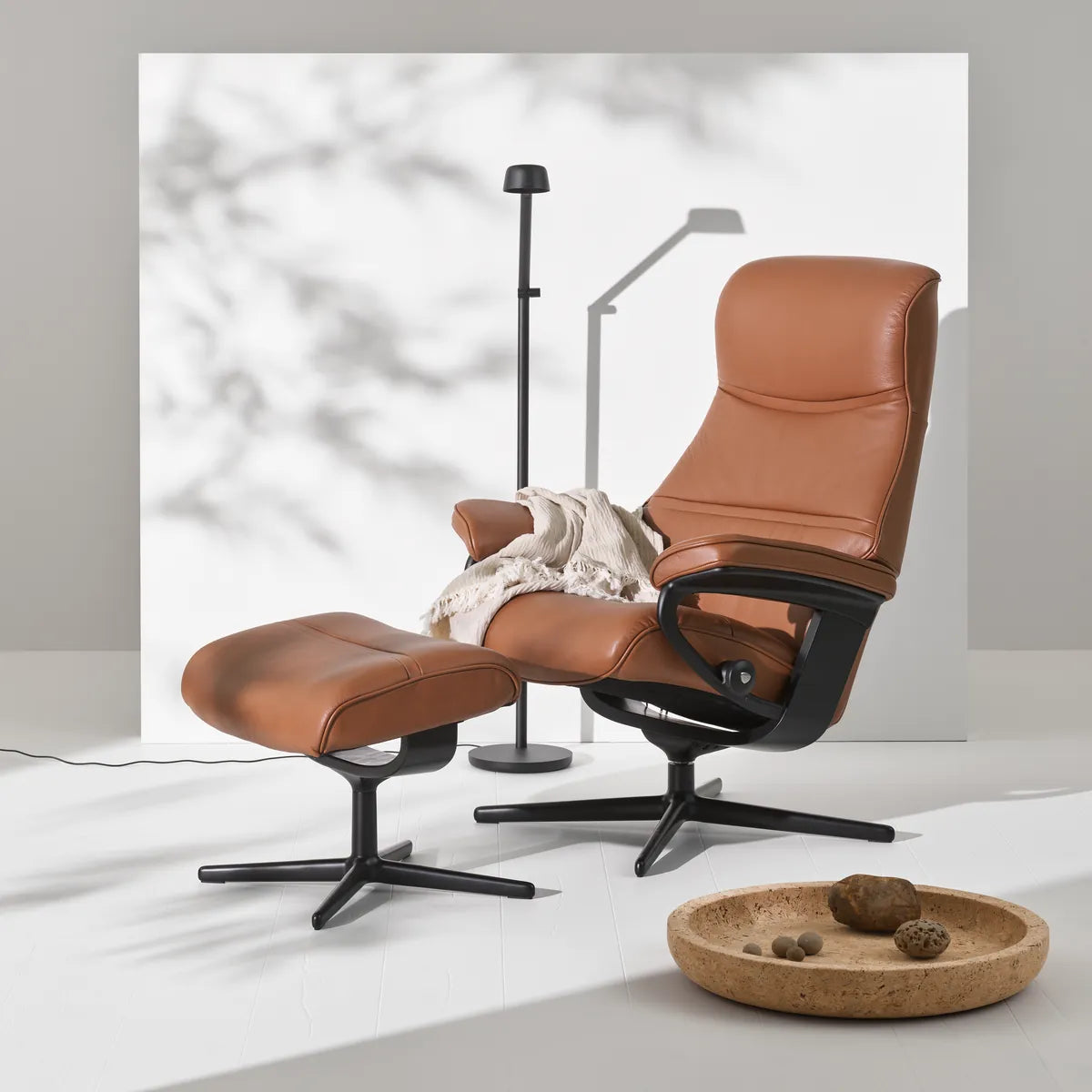Stressless Philip recliner with footstool in Velaro Dark Caramel leather on a matte black Cross base, in a bright studio