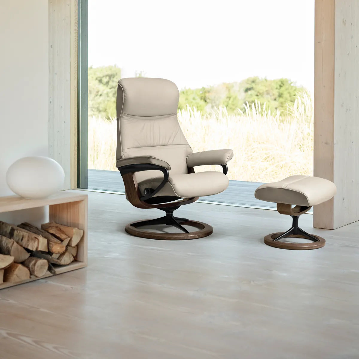 Stressless Philip with a footstool in Velaro Light Grey leather on a Signature base, in a bright living room with a view of nature