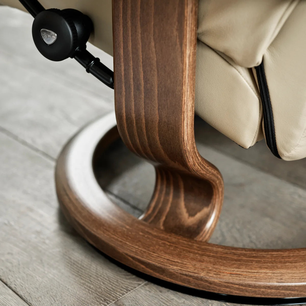 Detail van het Classic onderstel van de Stressless Sunrise in gelaagd walnoot, met de zandlopervorm en de verbinding met de zetel