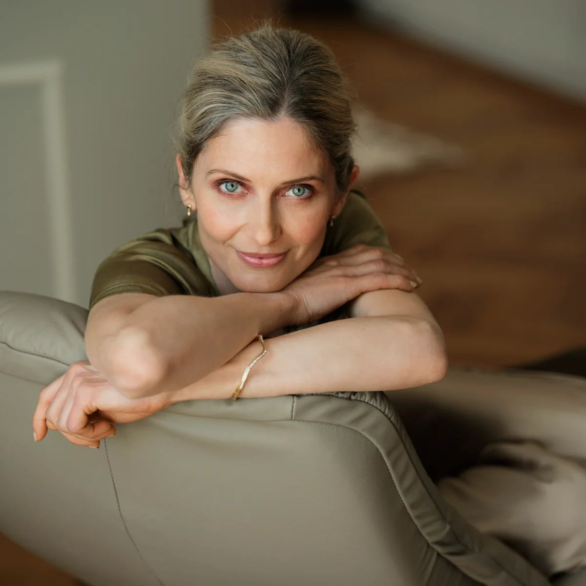 Vrouw leunt met haar armen op de gewelfde rugleuning van een Stressless Sunrise in Paloma Mushroom leder