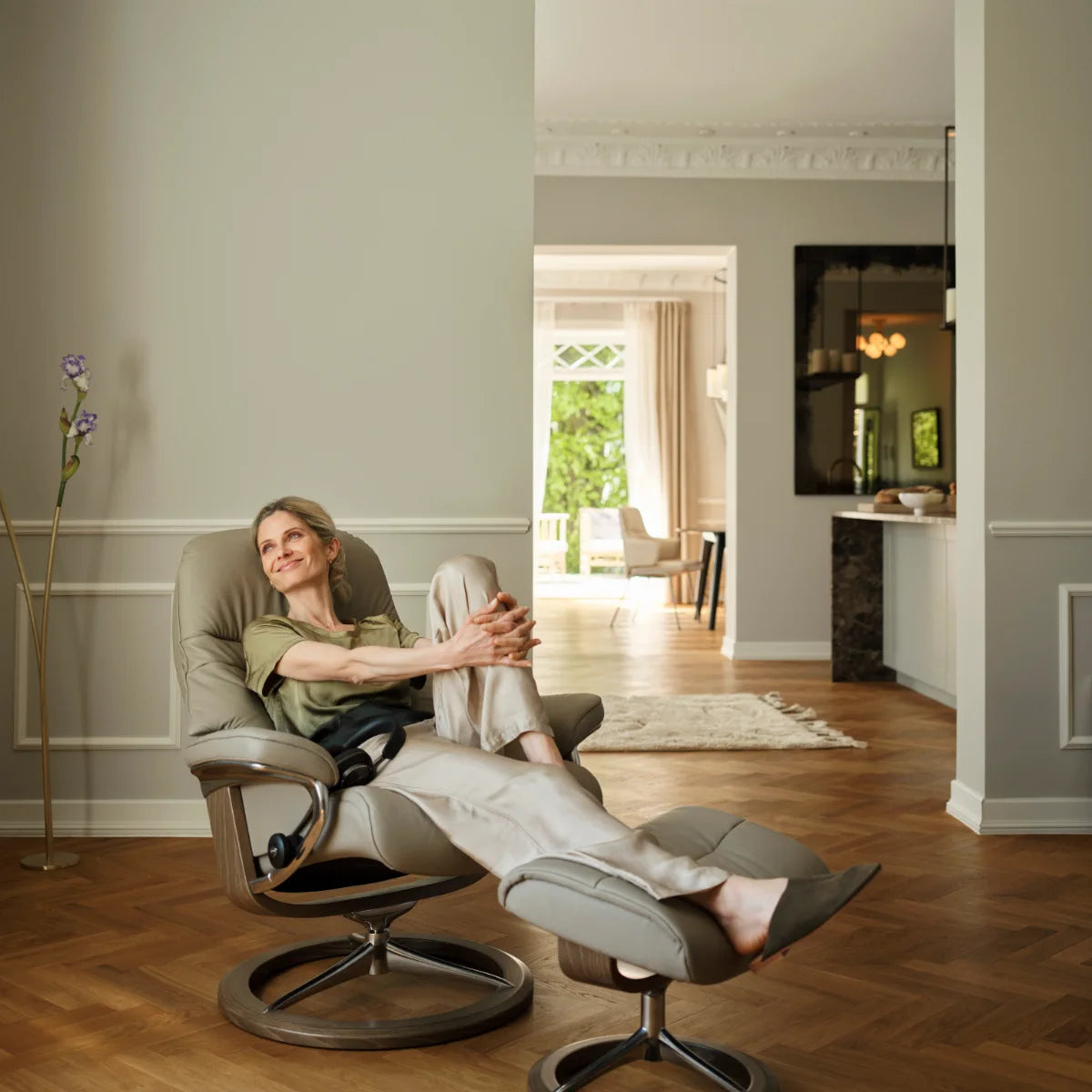 Vrouw ligt achterover in een Stressless Sunrise met de benen op de voetenbank, in een ruime woonkamer met parketvloer