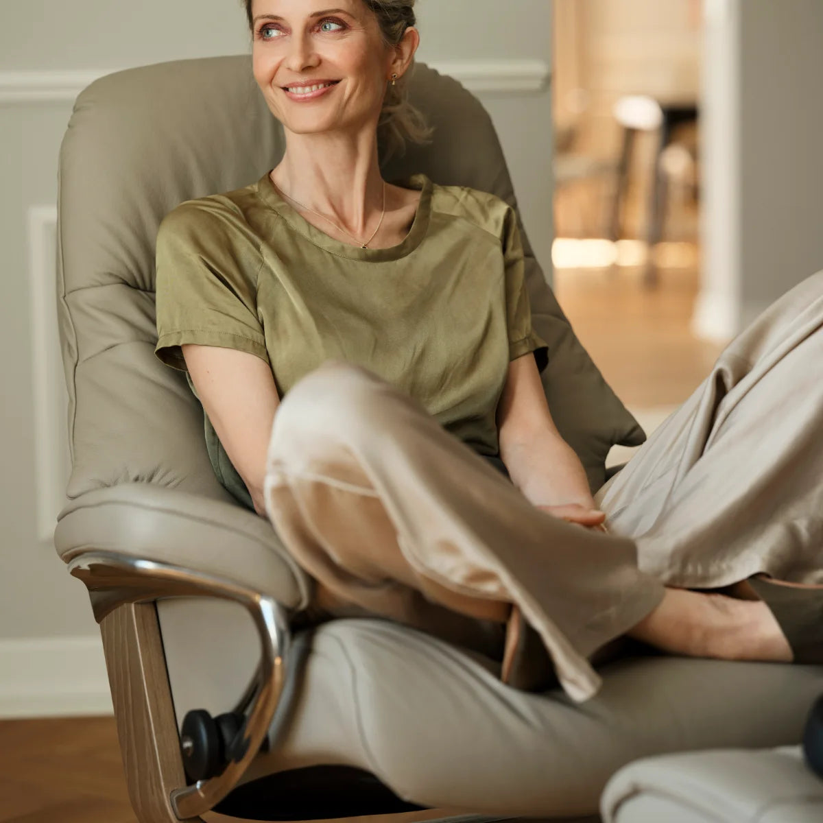 Vrouw zit ontspannen met opgetrokken benen in een Stressless Sunrise in Paloma Mushroom leder op een Signature onderstel