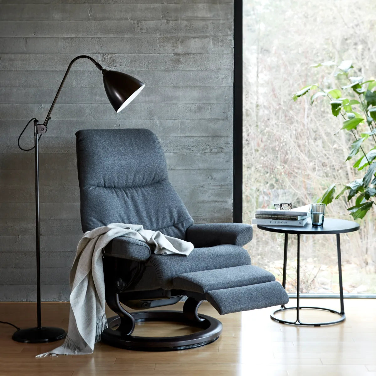 Stressless View Power in Calido Dark Grey stof op een Classic onderstel in wengé bij een betonnen wand
