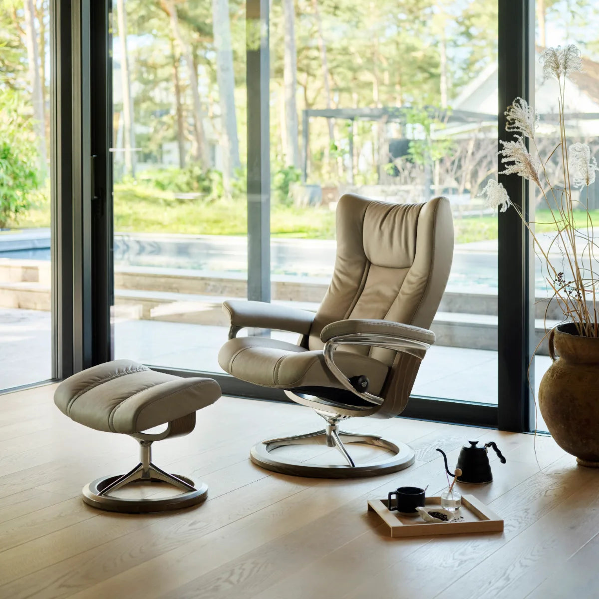 Stressless Wing in Paloma Mushroom leder met voetenbank op een Signature onderstel bij een groot raam